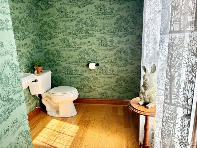half bathroom featuring baseboards, wallpapered walls, toilet, and wood finished floors