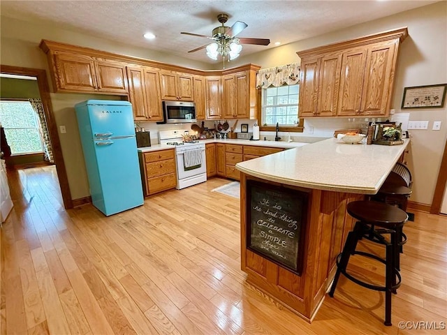 kitchen with stainless steel microwave, white range with gas cooktop, a peninsula, freestanding refrigerator, and brown cabinetry