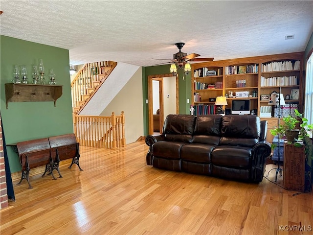 living room with a textured ceiling, wood finished floors, a ceiling fan, and visible vents
