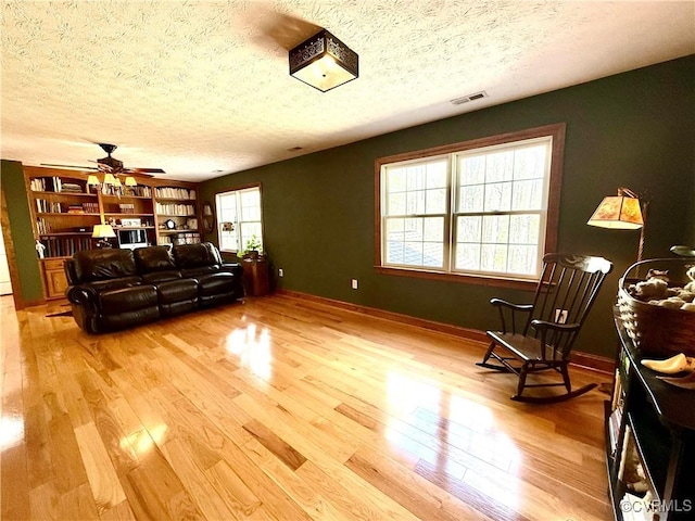 living room featuring light wood-style floors, visible vents, a textured ceiling, and a ceiling fan