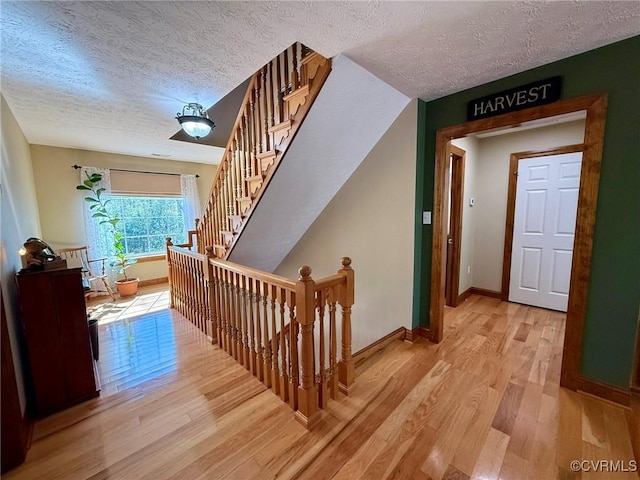 stairway with a textured ceiling, wood finished floors, and baseboards