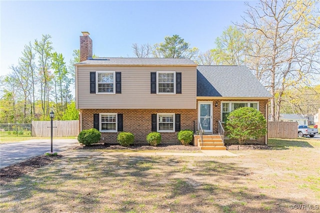 tri-level home featuring brick siding, fence, and a chimney