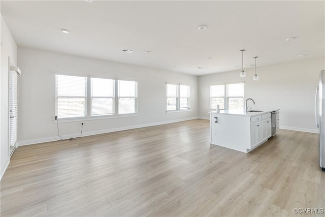 unfurnished living room featuring light wood-style flooring, visible vents, baseboards, and a sink