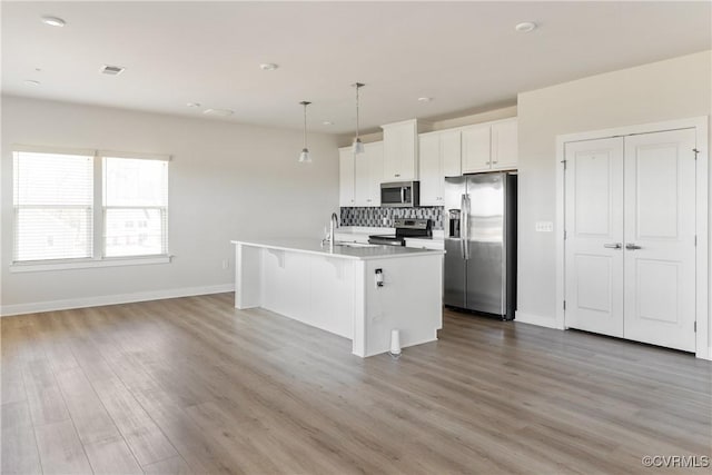 kitchen featuring stainless steel appliances, backsplash, wood finished floors, a breakfast bar, and an island with sink