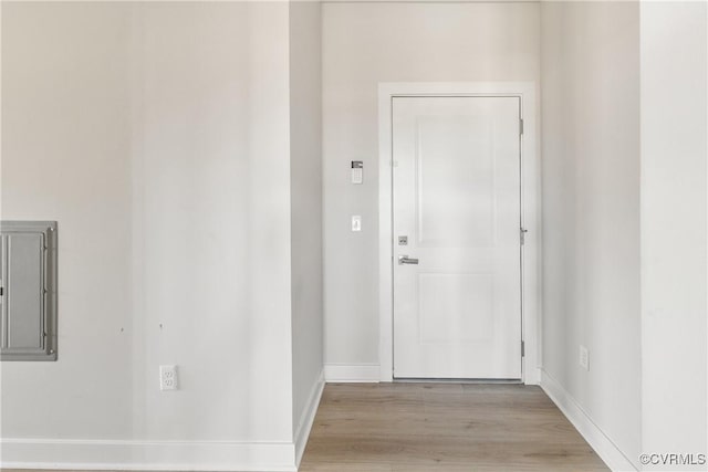 corridor featuring electric panel, baseboards, and light wood-style floors