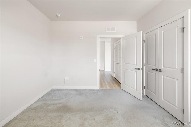unfurnished bedroom featuring visible vents, baseboards, a closet, and light colored carpet