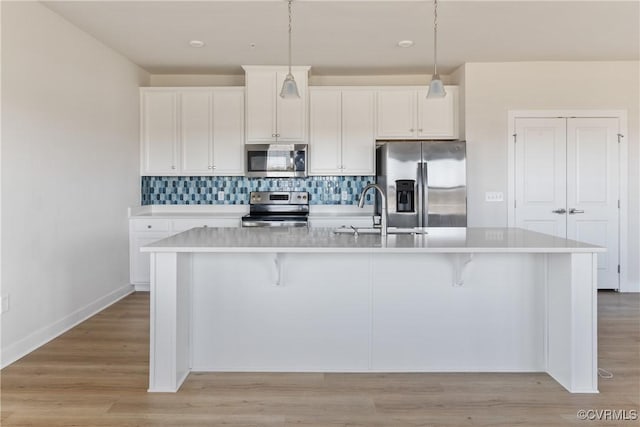 kitchen featuring white cabinets, an island with sink, stainless steel appliances, light countertops, and a sink