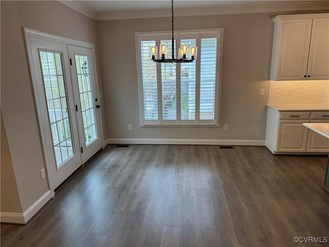 unfurnished dining area with crown molding, dark wood finished floors, visible vents, a notable chandelier, and baseboards