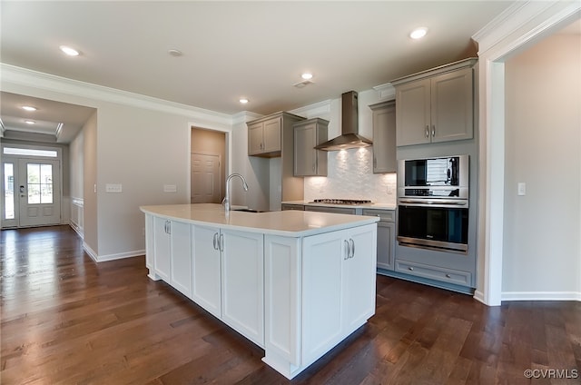 kitchen featuring wall chimney range hood, light countertops, gray cabinets, stainless steel appliances, and a center island with sink