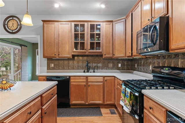 kitchen featuring black appliances, a sink, light countertops, decorative backsplash, and light wood-style flooring