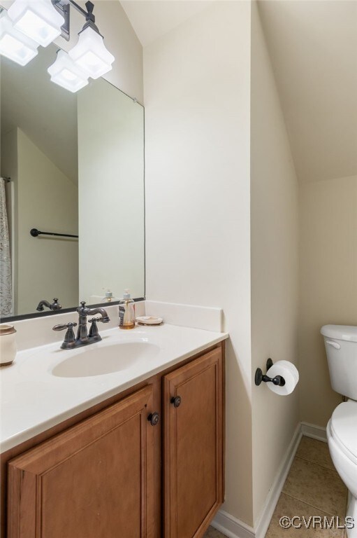 bathroom with toilet, vaulted ceiling, tile patterned floors, vanity, and baseboards