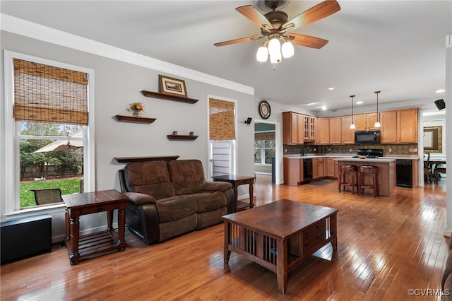 living area featuring healthy amount of natural light, light wood-type flooring, a ceiling fan, crown molding, and recessed lighting
