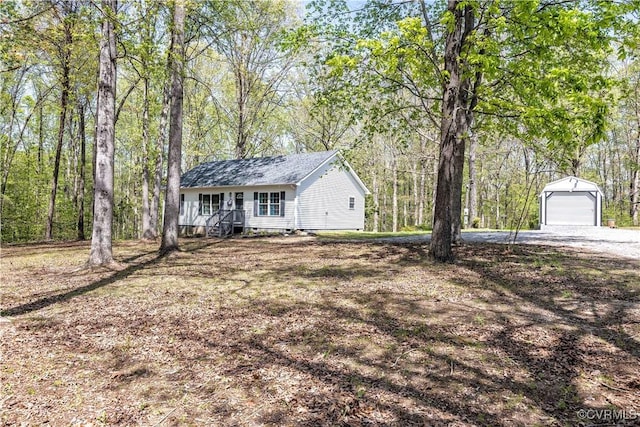ranch-style house featuring a garage, dirt driveway, a view of trees, and an outdoor structure