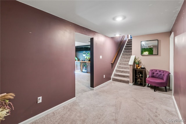 sitting room with baseboards, wine cooler, stairway, and light colored carpet