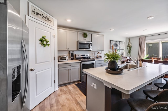 kitchen featuring a sink, a breakfast bar, stainless steel appliances, light countertops, and gray cabinetry
