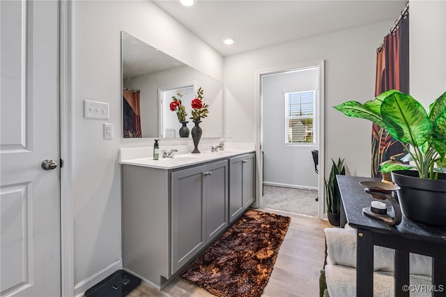 bathroom with recessed lighting, double vanity, wood finished floors, a sink, and baseboards