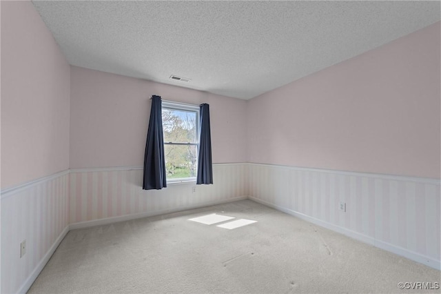 spare room with a textured ceiling, carpet, wainscoting, and visible vents