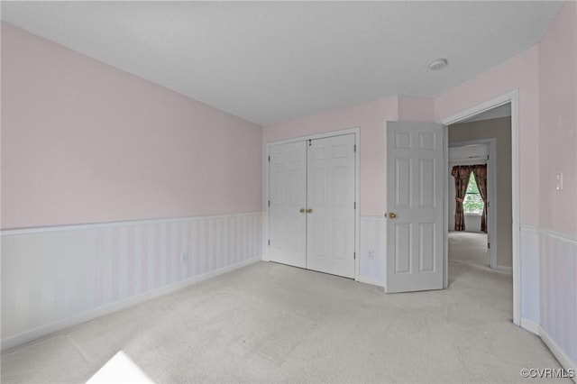 unfurnished bedroom featuring light carpet, a closet, and wainscoting