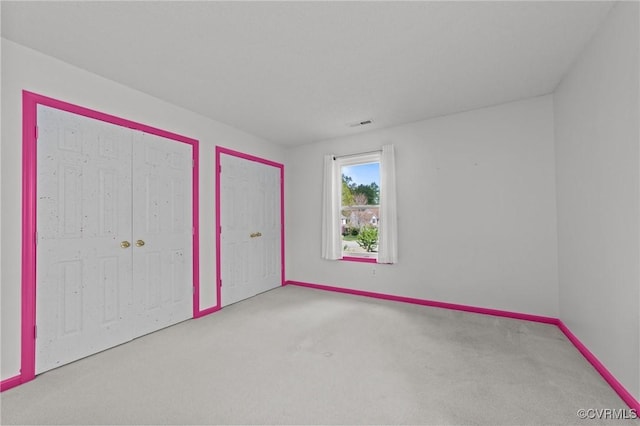 unfurnished bedroom featuring visible vents, baseboards, multiple closets, and carpet floors