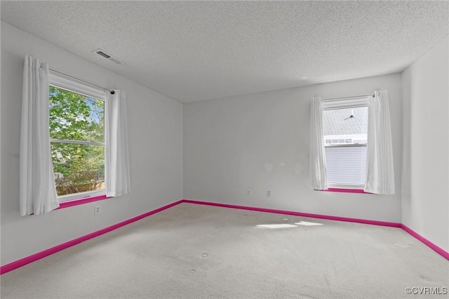 carpeted spare room with a textured ceiling, baseboards, and visible vents