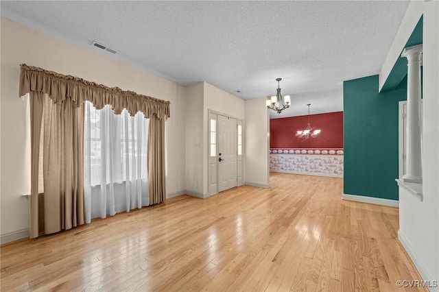 entrance foyer featuring visible vents, an accent wall, a chandelier, hardwood / wood-style flooring, and a textured ceiling