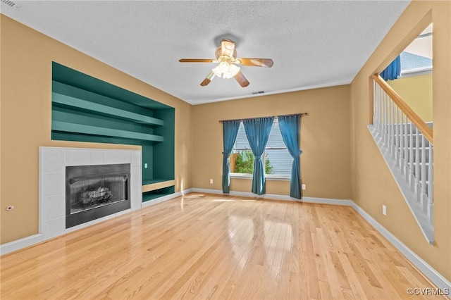 unfurnished living room featuring baseboards, ceiling fan, a textured ceiling, wood finished floors, and a tile fireplace