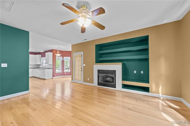 unfurnished living room featuring a tiled fireplace, baseboards, a ceiling fan, and light wood-style floors