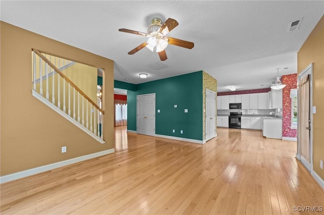 unfurnished living room with visible vents, light wood-style flooring, baseboards, and stairs