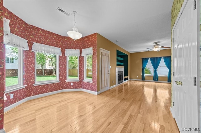 unfurnished living room with visible vents, baseboards, ceiling fan, wallpapered walls, and wood-type flooring