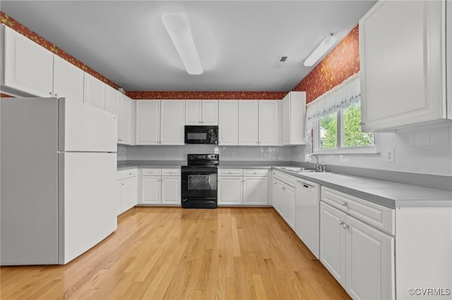 kitchen with white cabinets, light wood-style floors, a sink, and black appliances