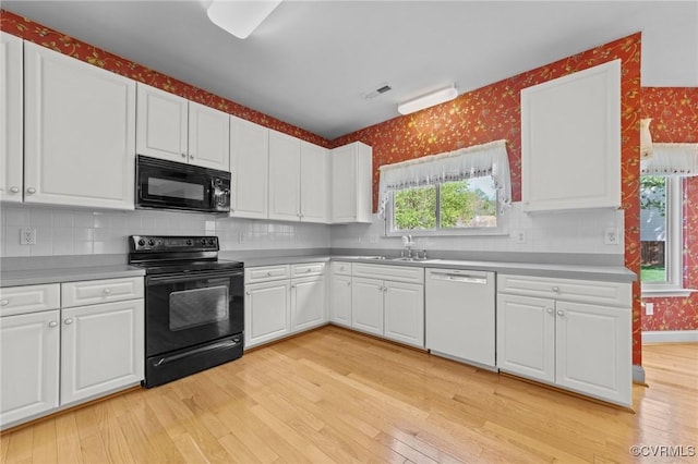 kitchen with wallpapered walls, visible vents, a sink, and black appliances