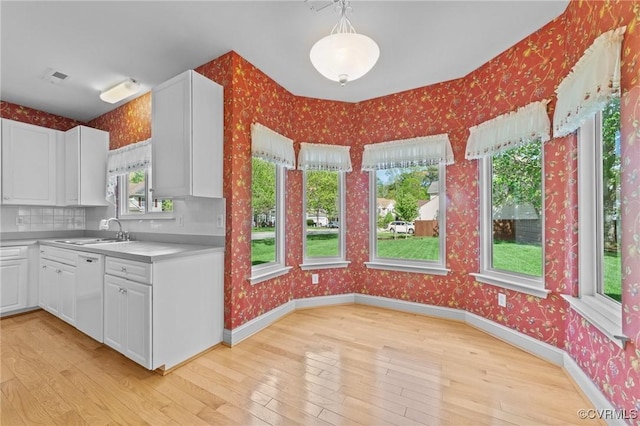 kitchen featuring wallpapered walls, light wood finished floors, a sink, and white dishwasher