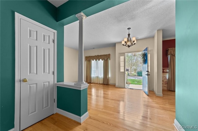 foyer entrance with a chandelier, light wood finished floors, a textured ceiling, and baseboards