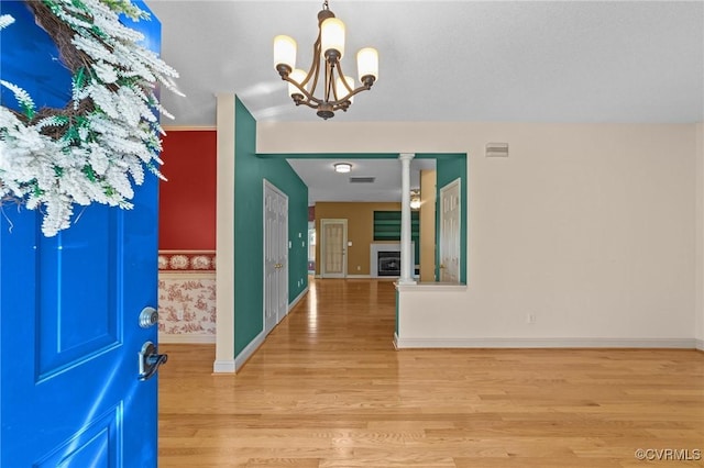 foyer entrance featuring an inviting chandelier, decorative columns, light wood-type flooring, visible vents, and baseboards