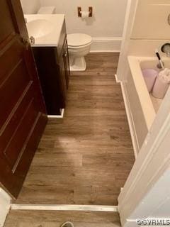 full bath featuring vanity, toilet, a bathtub, baseboards, and wood finished floors