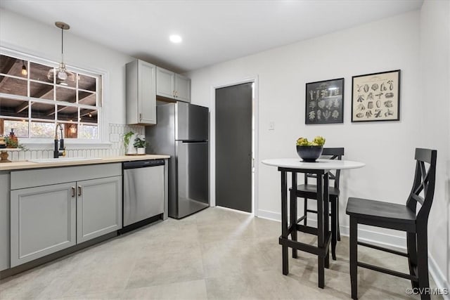 kitchen with stainless steel appliances, baseboards, gray cabinetry, and a sink