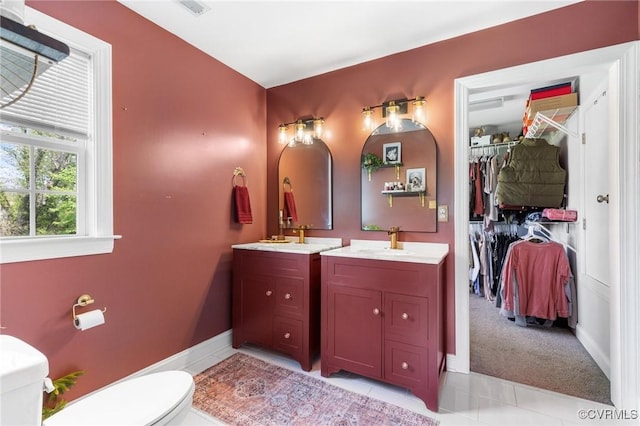 bathroom with tile patterned flooring, toilet, vanity, a walk in closet, and baseboards