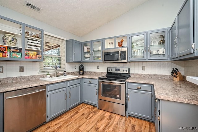 kitchen featuring a sink, stainless steel appliances, visible vents, vaulted ceiling, and a textured ceiling