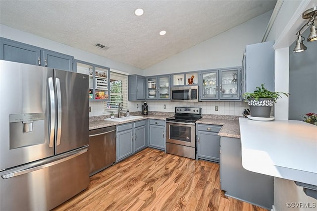 kitchen featuring a textured ceiling, a sink, appliances with stainless steel finishes, visible vents, and vaulted ceiling