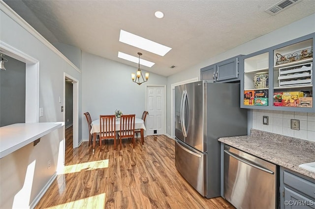 kitchen with lofted ceiling with skylight, tasteful backsplash, stainless steel appliances, and light wood-style floors