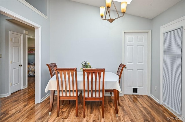 dining room with baseboards, wood finished floors, a notable chandelier, and vaulted ceiling