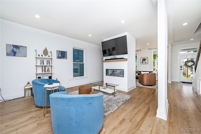 living room with recessed lighting, a glass covered fireplace, and light wood-style flooring