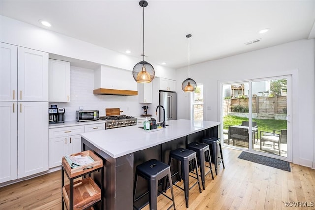 kitchen featuring stove, high quality fridge, visible vents, a sink, and custom exhaust hood