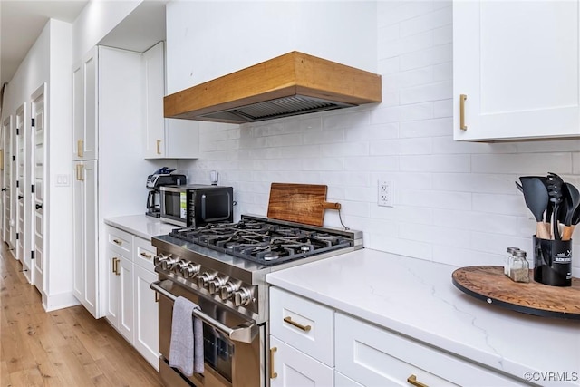 kitchen with tasteful backsplash, high end range, light wood-type flooring, white cabinets, and light stone countertops