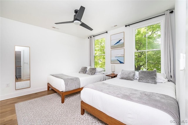 bedroom featuring wood finished floors, visible vents, a ceiling fan, and baseboards