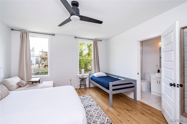 bedroom with a ceiling fan, ensuite bath, and light wood-style floors