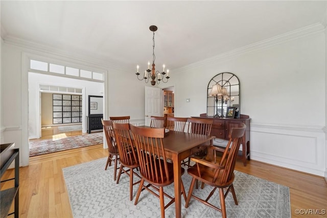 dining room featuring ornamental molding, wainscoting, wood finished floors, and a notable chandelier