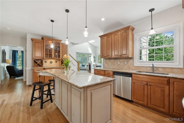 kitchen with stainless steel dishwasher, decorative backsplash, a center island, a sink, and light wood-style flooring