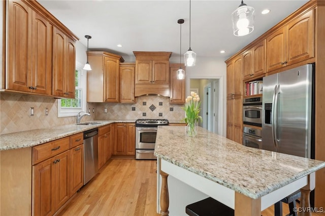 kitchen featuring a kitchen island, appliances with stainless steel finishes, light stone countertops, a sink, and light wood-style flooring