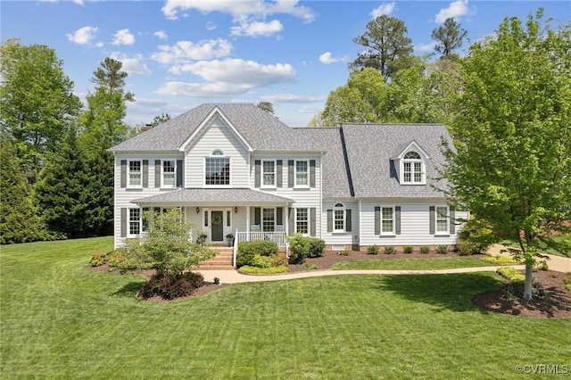 colonial house featuring covered porch, a shingled roof, and a front yard